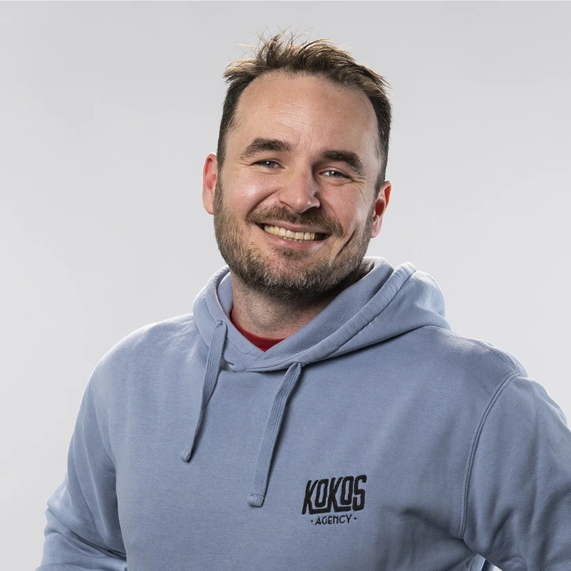 Portret nasmejanega sodelavca v svetlem puloverju z logotipom Kokos.